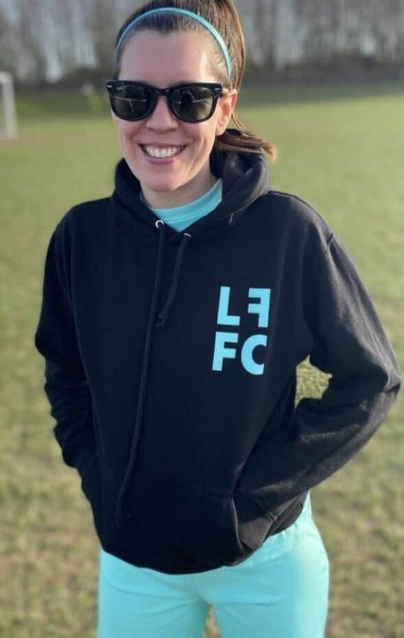 A supporter wearing the black club hoodie beside the pitch